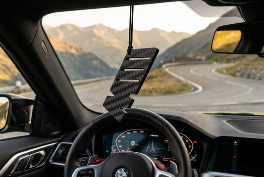 Ciondolo M nell’abitacolo di una BMW M4 con panorama montano